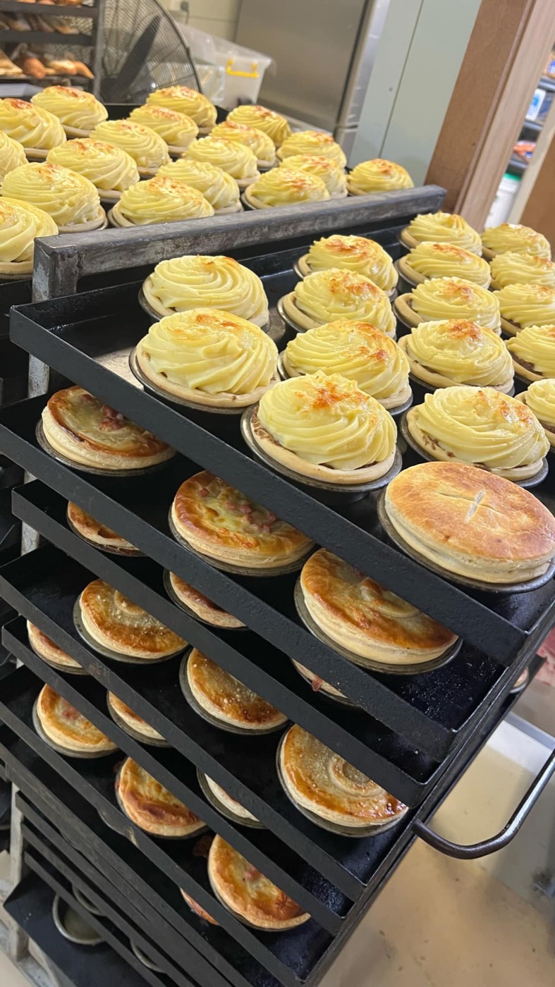 A baking rack of pies: some topped with piped swirls of mash, others with golden puff-pastry lids